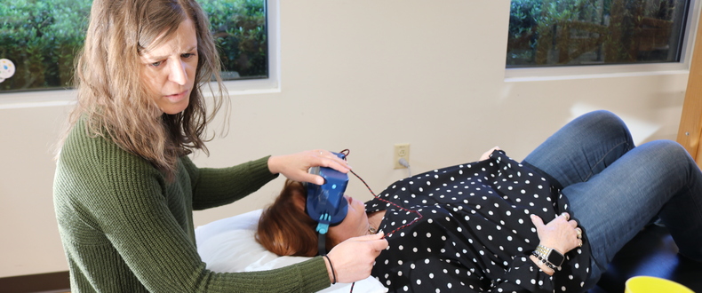 Clinician fitting a sensor headset on a person lying on an examination table in a medical clinic.
