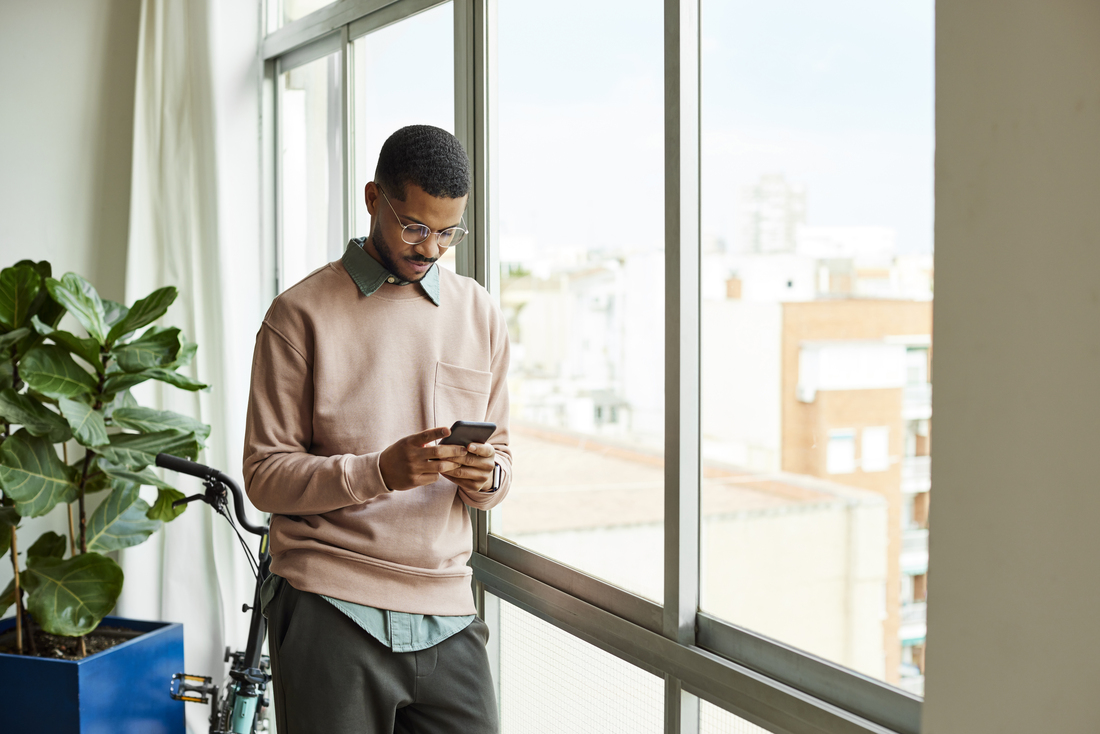 man standing at window dialing phone