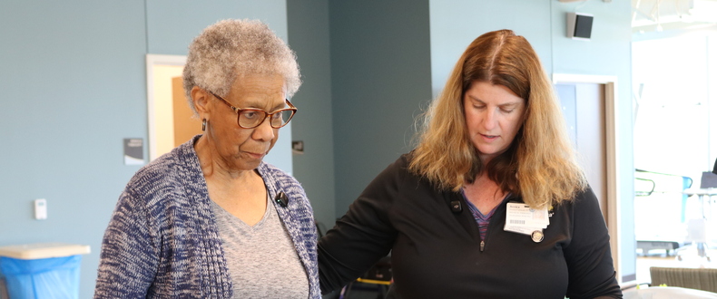 Physical therapist assisting an older adult during gait training with parallel bars and a support belt in a rehabilitation clinic.