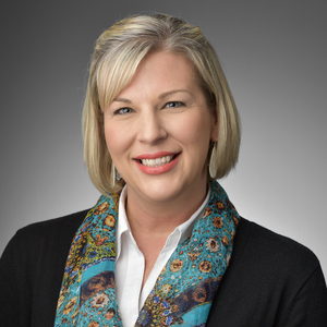 Professional portrait of Jenny Snodgrass, Vice President of Strategic Transformation at Sentara Health, wearing a patterned blue scarf and business attire against a neutral gray background.