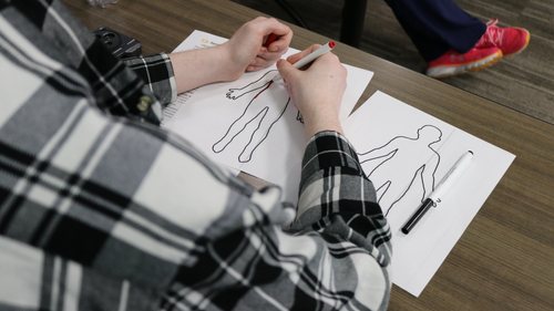 Close-up of a participant using markers to complete a body mapping exercise during a burn and trauma survivor support group session.