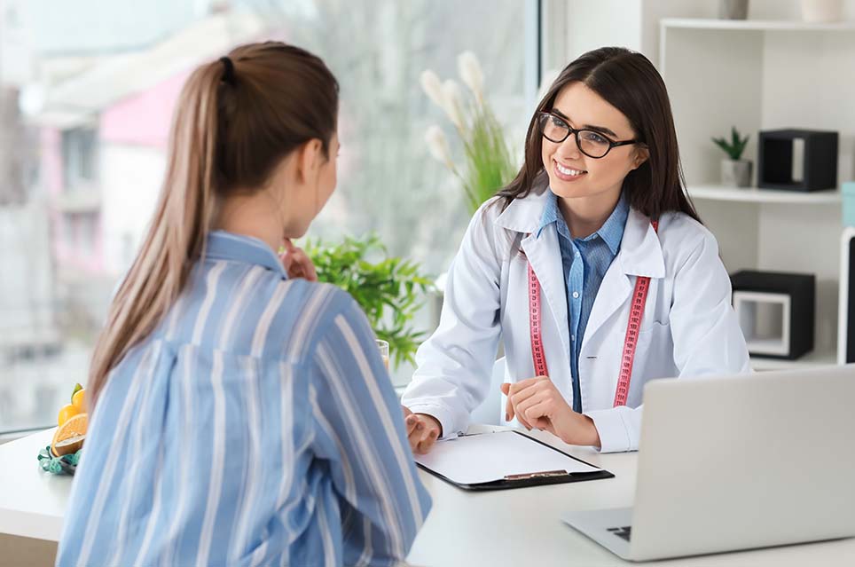 provider sitting at desk with clipboard smiling at another person sitting in front of her