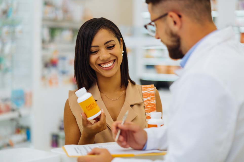 Woman Holding a Prescription Bottle and Talking to a Pharmacist