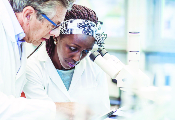 Researchers in lab coats examine samples using a microscope in a scientific laboratory setting.