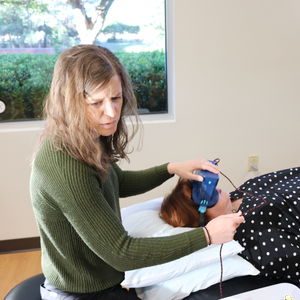 Clinician fitting a sensor headset on a person lying on an examination table in a medical clinic.