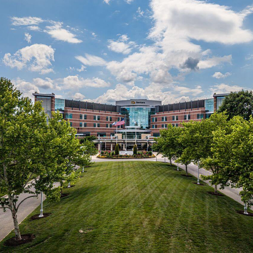 Sentara Williamsburg Regional Medical Center exterior with landscaped lawn, trees, and main hospital entrance under a blue sky.