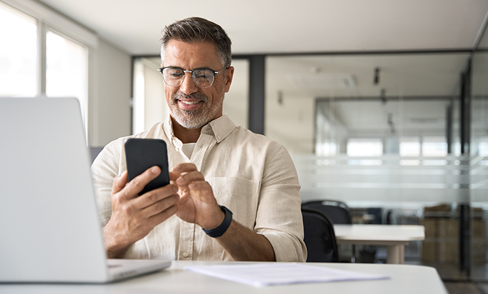 Man with smart phone sitting at a computer