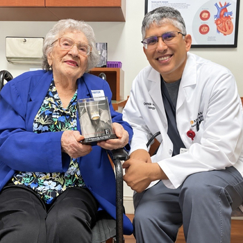 Older adult and healthcare provider seated in an exam room, holding a model of a heart valve implant.