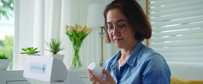 woman wearing glasses holding a medication bottle, reading the instructions