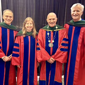 Four academic leaders wearing red doctoral regalia pose together at a commencement or academic ceremony.