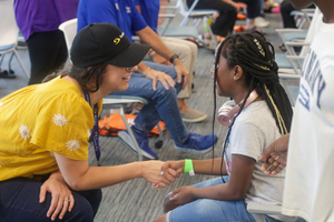A Sentara volunteer sits in a chair directly across from a young girl and shakes her hand during the Shoes of Hope event at the ForKids Landmark Center in Chesapeake.