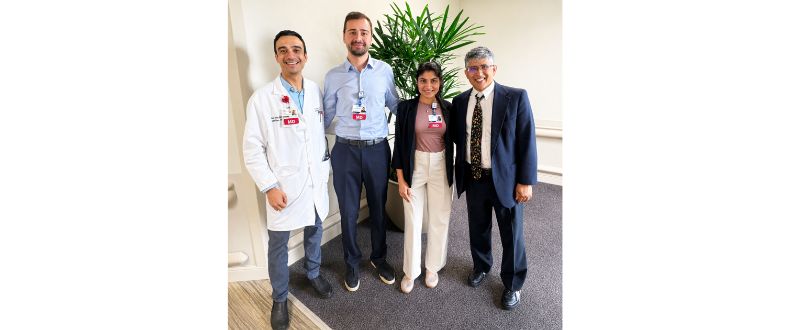 Four doctors standing together in a hospital hallway, posing for a group photo near a large indoor plant.