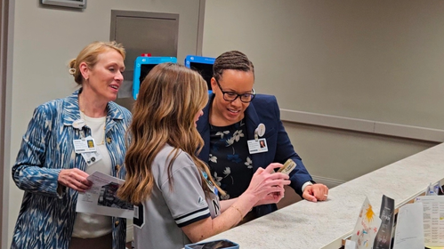 Melinda Hancock (left), Sentara’s first female chief finance officer, and Graves (right) watch as Tara Silvestri (center), nurse manager of labor and delivery at Sentara Norfolk General Hospital, shows them photos of Hospital Week celebrations