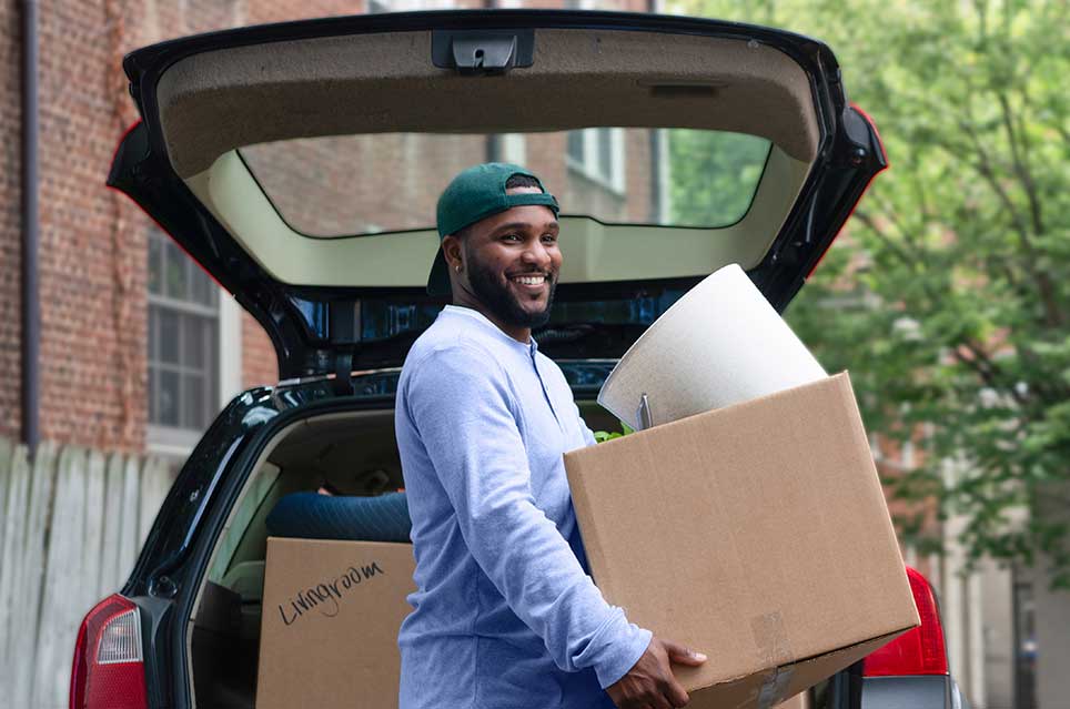 man carrying a box in front of a hatchback car