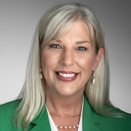 Professional portrait of Jenny Snodgrass, Vice President of Strategic Transformation at Sentara Health, wearing a patterned blue scarf and business attire against a neutral gray background.