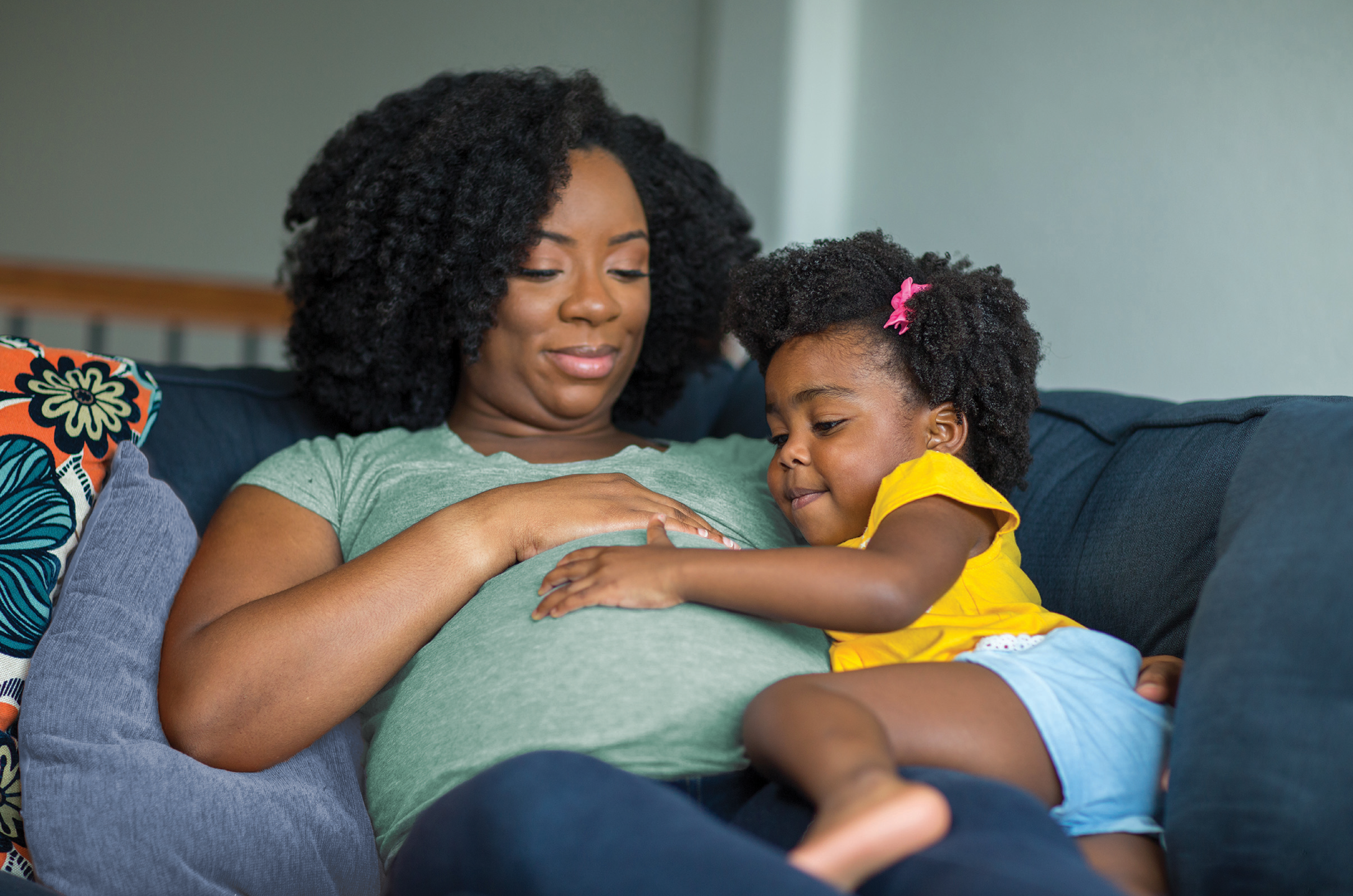 pregnant mother laying on couch with young daughter