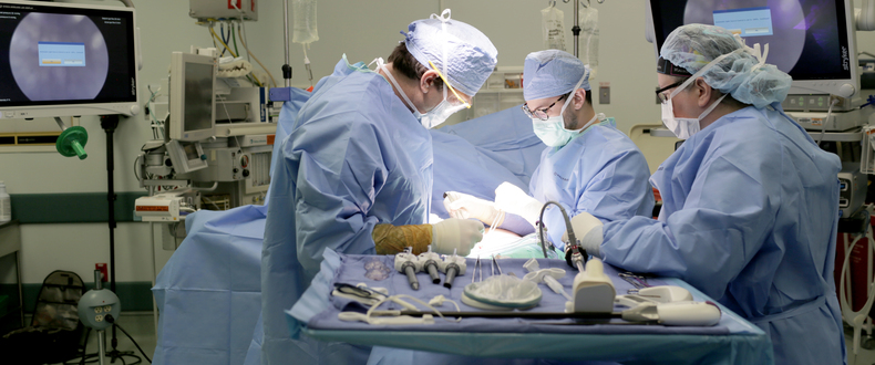 Surgical team performing a procedure in a modern operating room with overhead lights and medical monitors