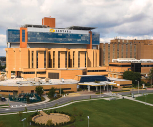 Exterior view of a multi-story Sentara hospital campus featuring a modern glass and brick tower, landscaped grounds, and a covered main entrance.