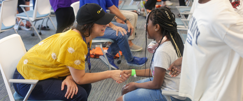 A Sentara volunteer sits in a chair directly across from a young girl and shakes her hand during the Shoes of Hope event at the ForKids Landmark Center in Chesapeake.
