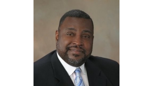 Professional headshot of Thomas Hasty III wearing a dark suit, white shirt, and light blue patterned tie against a neutral background.