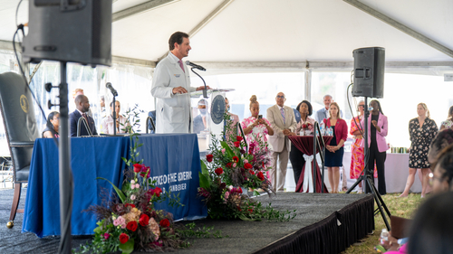 Michael Hooper, M.D., chief clinical officer for Sentara Health, speaks at a podium during the Queen Candis Sickle Cell Act of Virginia bill signing ceremony at the Sentara Community Care Center in Newport News, Thursday, June 11, 2026. Elected officials, community advocates, and healthcare leaders are seated and standing in the background beneath a large tent.