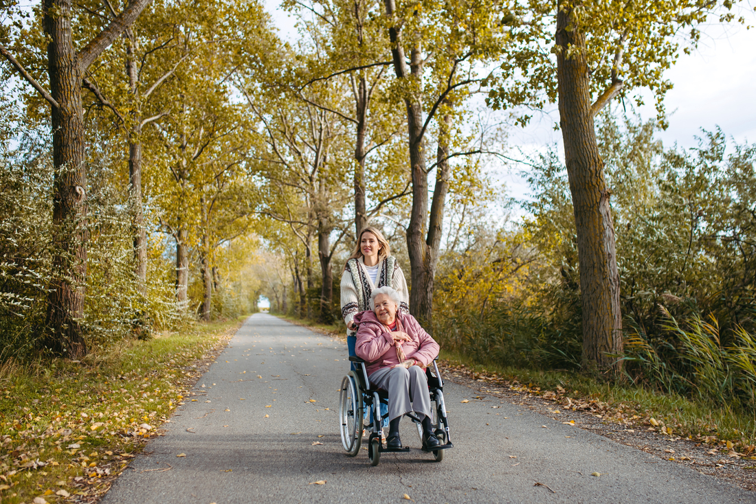 caregiver pushing wheelchair on autumn walk