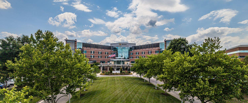 Sentara Williamsburg Regional Medical Center exterior with landscaped lawn, trees, and main hospital entrance under a blue sky.