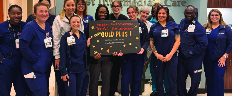 Clinical team members stand together in a hospital lobby holding an American Heart Association Get With The Guidelines® Stroke Gold Plus award sign in recognition of stroke care excellence.