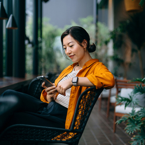 Person using a smartphone while seated on a patio surrounded by plants in an outdoor lounge setting.