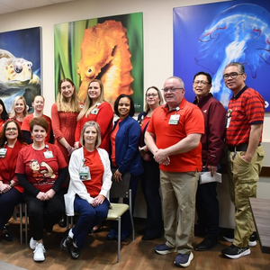 Group of healthcare workers at Sentara Virginia Beach General Hospital pose for a photo in front of pictures of aquatic animals. They are all wearing red to celebrate Heart Month.
