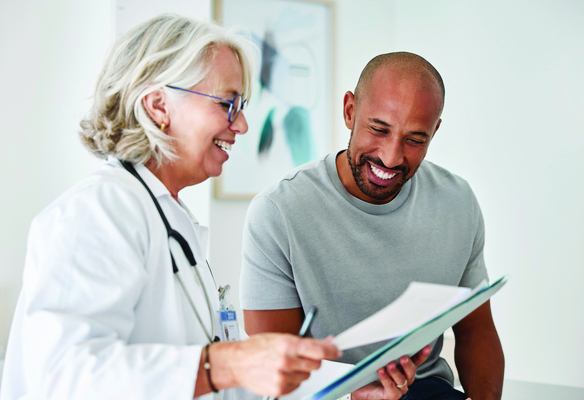 A healthcare professional reviews paperwork with an adult seated beside them, holding a clipboard and discussing information in a bright clinical office.