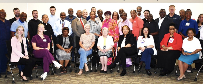 Group photo of approximately 30 faith leaders, healthcare professionals, and community members gathered indoors during a Sentara Faith Leaders Collaborative meeting.