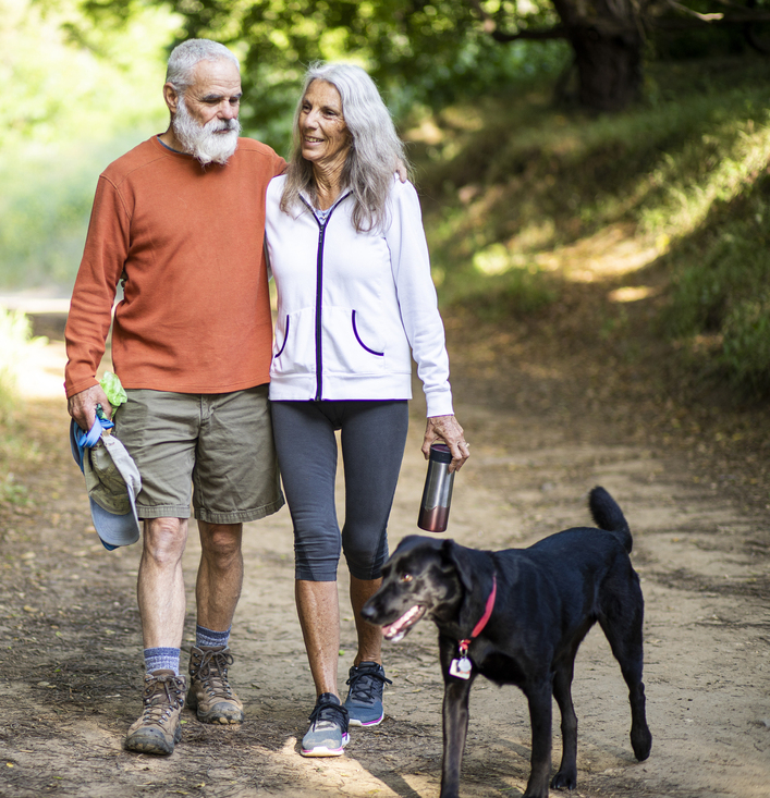 senior couple walking dog in woods