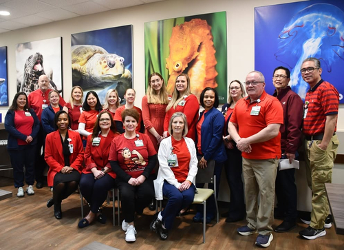 Group of healthcare workers at Sentara Virginia Beach General Hospital pose for a photo in front of pictures of aquatic animals. They are all wearing red to celebrate Heart Month.