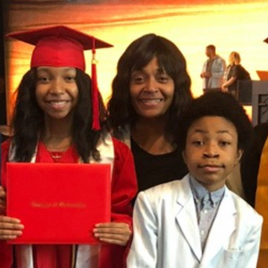Moneka Hemby poses with her four children at a graduation ceremony, three of them are in cap and gown.