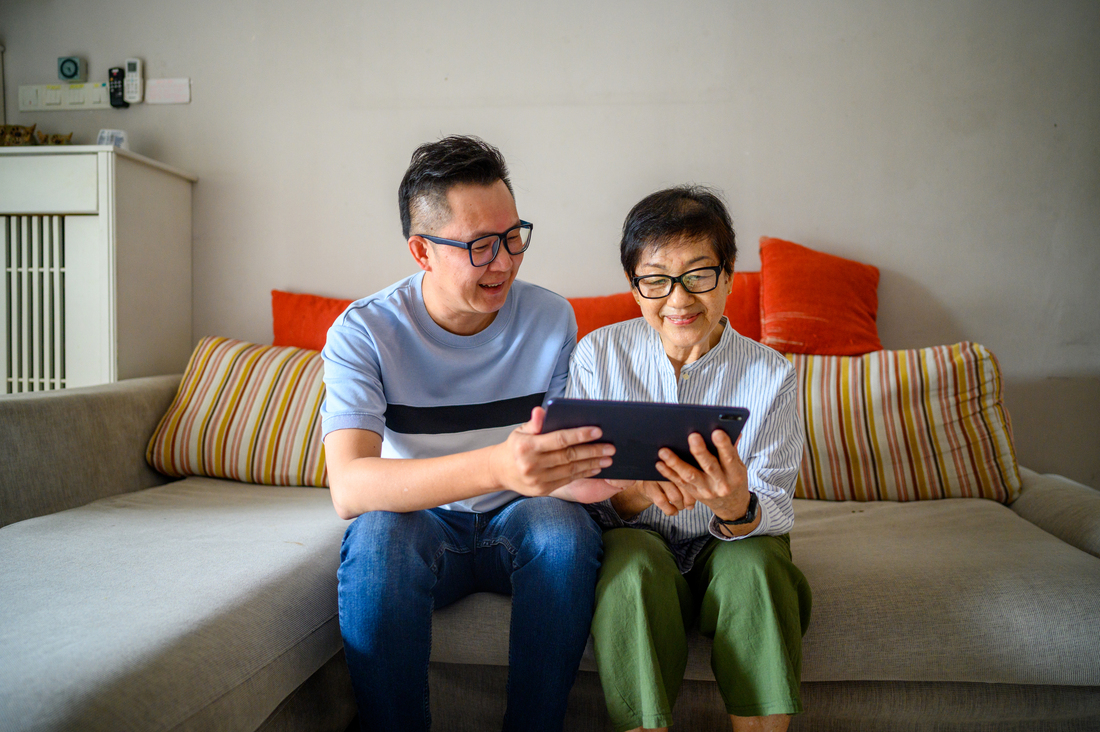 son helping elderly mother with tablet