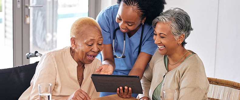 two elder women talking to a nurse looking at an ipad