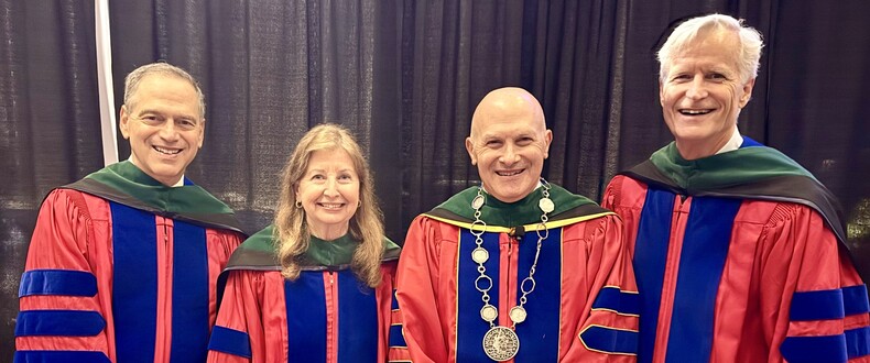 Four academic leaders wearing red doctoral regalia pose together at a commencement or academic ceremony.