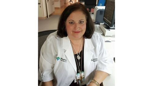 Kathleen Zechmeister, a longtime nurse and the inspiration behind Kathleen’s Angels, the nursing honor guard at Sentara Norfolk General Hospital, sits at a nursing station in a hospital setting wearing a white uniform.