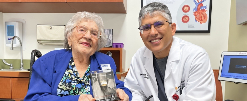 Older adult and healthcare provider seated in an exam room, holding a model of a heart valve implant.