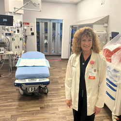 Breast cancer survivor Andrea Helmbach, MSN, APRN, AGACNP-BC, SCRN, is standing in one of the trauma treatment rooms in the Sentara Northern Virginia Medical Center emergency department, where she serves as Stroke Manager for Patient Care.
