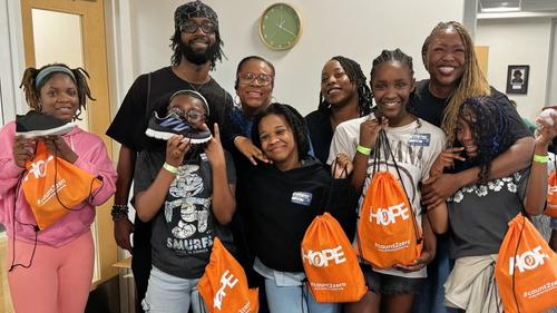 Children and their families smile for a group photo at the Shoes of Hope event at the ForKids Landmark Center in Chesapeake. Several children hold their new shoes and orange H.O.P.E. bags provided as part of the back-to-school event.